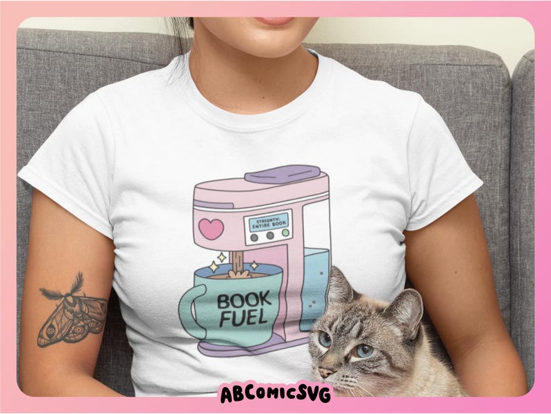 May include: White t-shirt featuring a pink coffee maker with a heart and the text "STRONK ENTIRE BOOK". A blue mug with "BOOK FUEL" is under the coffee maker. A cat with blue eyes is in the image.