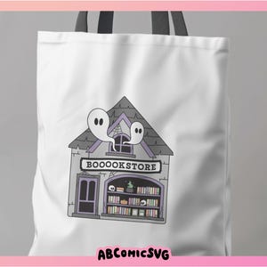 Pu&ograve; includere: Una borsa tote bianca con un manico nero presenta un'illustrazione a cartone animato di una libreria spettrale con un cartello che recita "BOOOKSTORE". Due fantasmi galleggiano sopra l'edificio.
