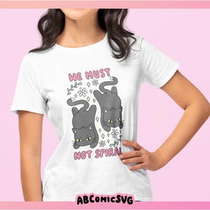 May include: White t-shirt featuring a cartoon design of two gray cats with yellow eyes, surrounded by flowers. The text "HE MUST NOT SPIRAL" is above the cats. The brand name "ABCOMICSVG" is at the bottom.