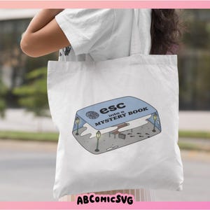 May include: White tote bag with a blue and white illustration of a game cartridge with the text "esc into a mystery book".