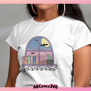 May include: White t-shirt with a cartoon window design. The window shows a moon, bats, and a cauldron. Books and candles sit on the sill. The text "ABCOMICSVG" is at the bottom of the image.