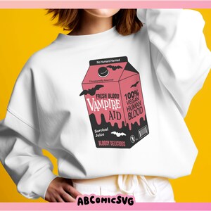 May include: A white sweatshirt with a graphic of a pink and black carton of "Fresh Blood Vampire Aid" with the text "100% Vegan Human Blood" and "Bloody Delicious".