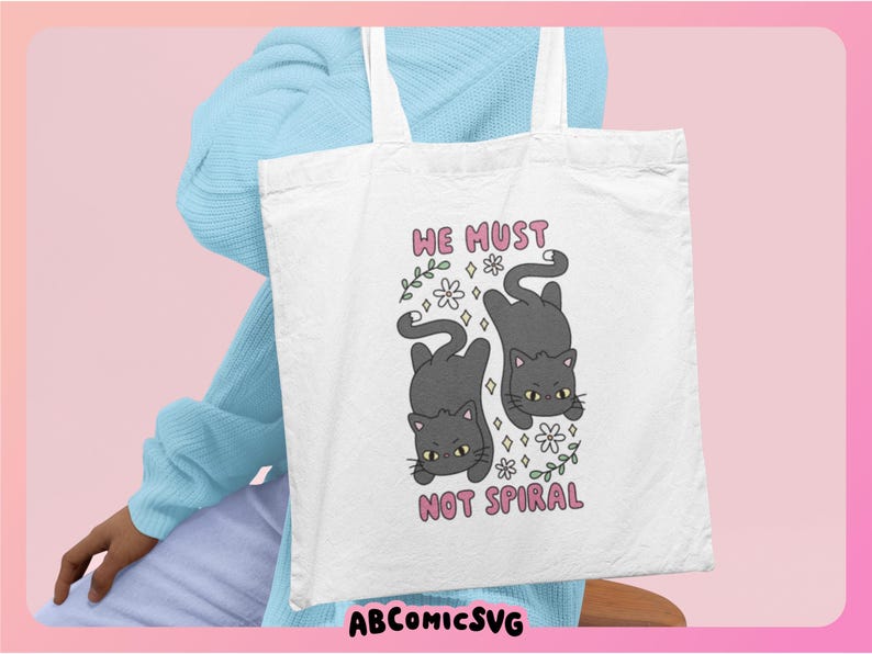May include: White tote bag featuring a cartoon design of two gray cats, flowers, and the text "WE MUST NOT SPIRAL" in pink. The bag has white handles and is held by a person wearing a light blue sweater.