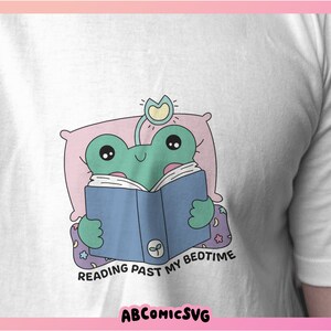 Op de afbeelding: Een groene kikker in een roze en witte nachtjapon leest een blauw boek met de tekst "Reading Past My Bedtime".
