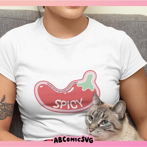 May include: A white t-shirt with a red and green chili pepper graphic that says "Spicy". A cat is sitting on the lap of the person wearing the shirt.