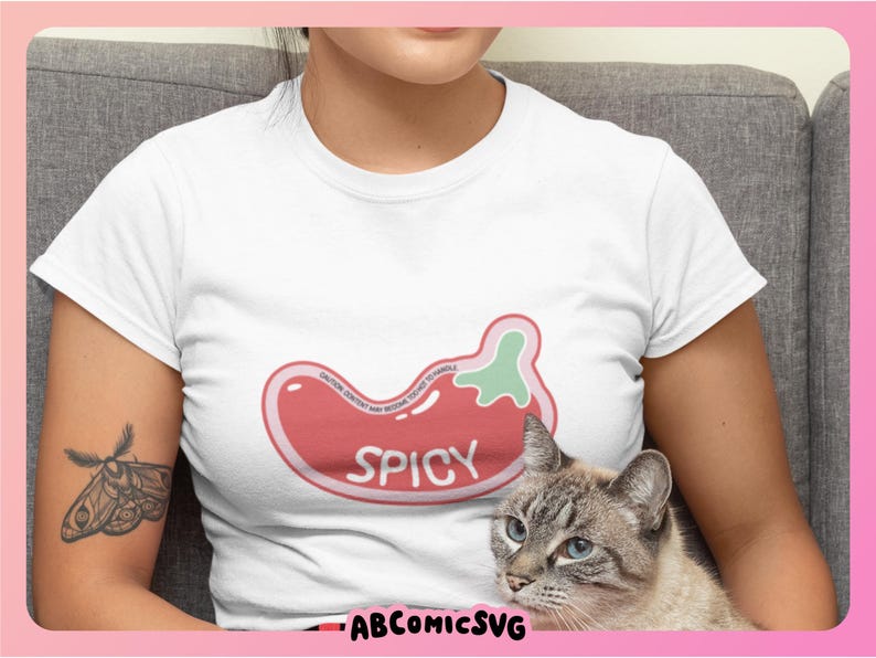 May include: A white t-shirt with a red and green chili pepper graphic that says "Spicy". A cat is sitting on the lap of the person wearing the shirt.