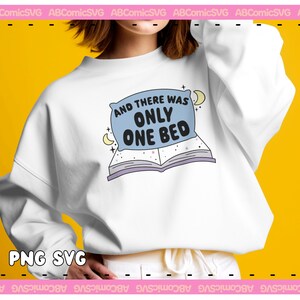 May include: White sweatshirt with a blue pillow and open book graphic. The text on the graphic reads "And there was only one bed."