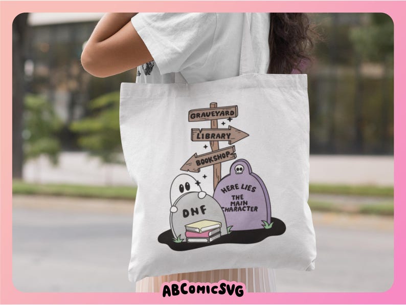 May include: White tote bag featuring a whimsical graveyard scene with tombstones, ghosts, and directional signs pointing to a graveyard, library, and bookshop. The text "Here Lies The Main Character" is on a tombstone. The bag also has the text "ABCOMICSVG".