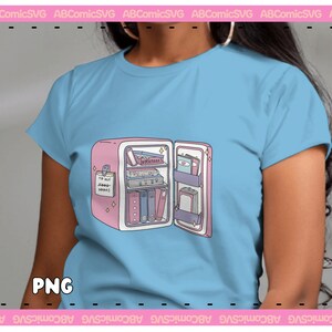 Pode incluir: Uma camiseta azul clara com um gr&aacute;fico de uma geladeira rosa cheia de livros. A geladeira tem uma nota na porta que diz "Para comprar mais livros".
