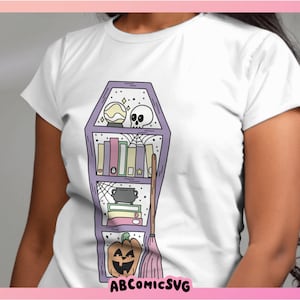 May include: A white t-shirt featuring a purple coffin-shaped bookshelf design. The bookshelf is filled with books, a cauldron, a skull, a crystal ball, and a broom. The text "ABCOMICSVG" is at the bottom of the design.