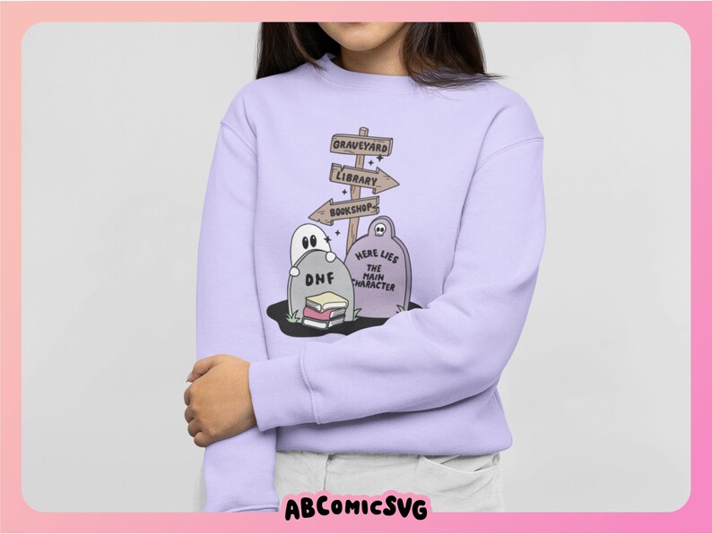 May include: A light purple sweatshirt featuring a graveyard scene with tombstones, a ghost, and directional signs pointing to a graveyard, library, and bookshop. The text "Here Lies The Main Character" is on a tombstone. The design is whimsical and cartoonish.