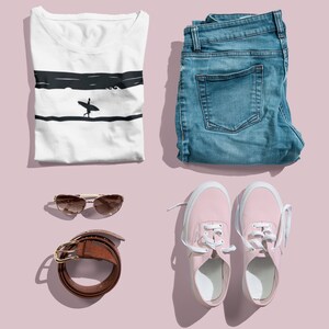 K&ouml;nnte beinhalten: Eine flache Anordnung eines l&auml;ssigen Outfits mit einem wei&szlig;en T-Shirt mit einem Surfer-Motiv, einer blauen Jeans, rosa Sneakern, einem braunen G&uuml;rtel und einer Sonnenbrille.