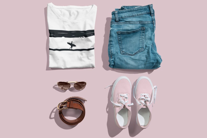 K&ouml;nnte beinhalten: Eine flache Anordnung eines l&auml;ssigen Outfits mit einem wei&szlig;en T-Shirt mit einem Surfer-Motiv, einer blauen Jeans, rosa Sneakern, einem braunen G&uuml;rtel und einer Sonnenbrille.