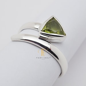 Op de afbeelding: Een zilveren ring met een groene edelsteen in een driehoekige vorm. De ring is ontworpen om om de vinger te wikkelen.