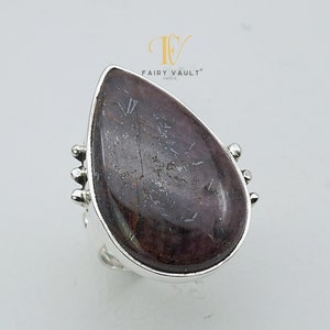 Puede incluir: Un anillo de plata con una piedra preciosa de color púrpura oscuro en forma de lágrima. La piedra preciosa tiene un patrón único y moteado.