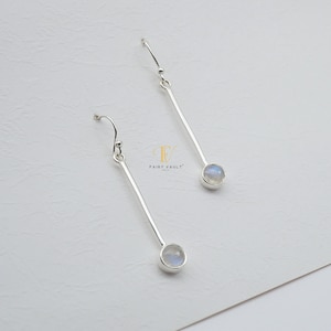May include: A pair of silver dangle earrings with a moonstone gemstone at the end of each earring.
