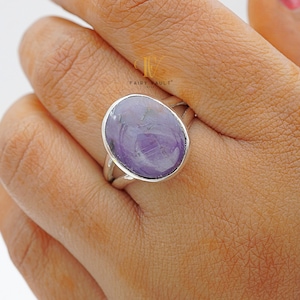May include: A silver ring featuring a large oval amethyst gemstone. The gemstone is a light purple colour with swirls of darker purple.