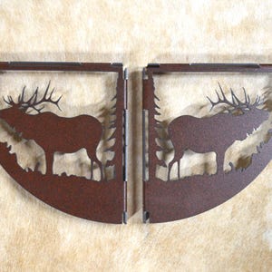 May include: Two rusty metal shelf brackets shaped like a half-circle with an elk silhouette inside. The elk is facing left on the left bracket and right on the right bracket.