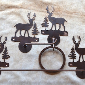 May include: A set of three rustic metal towel racks featuring a silhouette of a deer and a pine tree. The towel racks are designed to hold towels, hand towels, and washcloths.