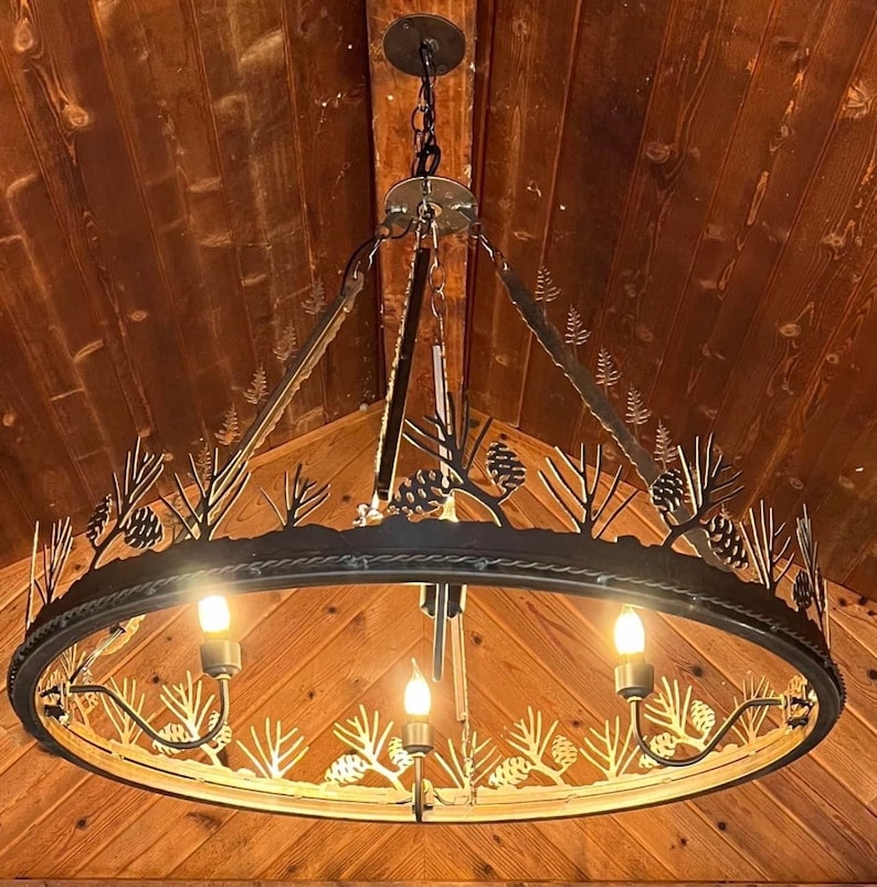 May include: A round, black metal chandelier with a rustic design featuring pine tree silhouettes. The chandelier has four light bulbs and is hanging from a wooden ceiling.