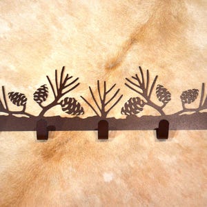 May include: A brown metal coat rack with six hooks shaped like pine branches and pine cones. The rack is mounted on a wall.