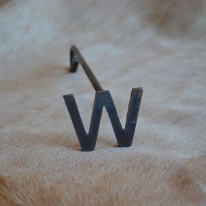 May include: A metal branding iron shaped like the letter W. The iron is black and has a long handle.