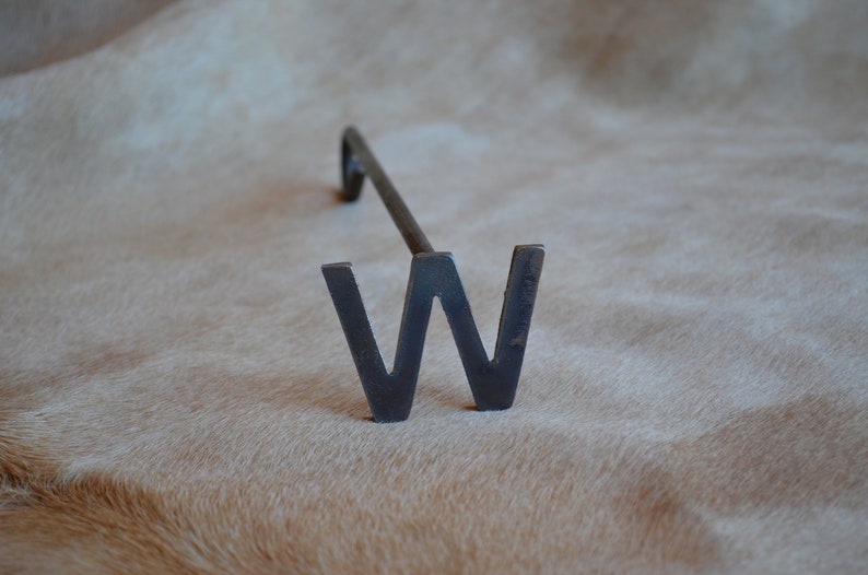 May include: A metal branding iron shaped like the letter W. The iron is black and has a long handle.