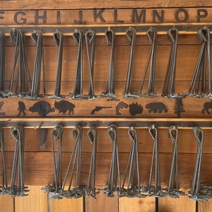 May include: A wooden wall display with two rows of metal hooks. Each hook holds a bundle of metal skewers. The top row is labeled with the letters A through T. The bottom row is labeled with the letters U through Z. The wall is decorated with a row of animal silhouettes.