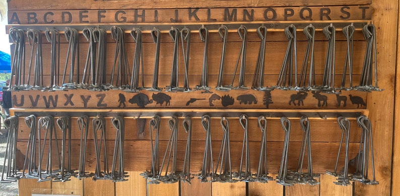 May include: A wooden wall display with two rows of metal hooks. Each hook holds a bundle of metal skewers. The top row is labeled with the letters A through T. The bottom row is labeled with the letters U through Z. The wall is decorated with a row of animal silhouettes.