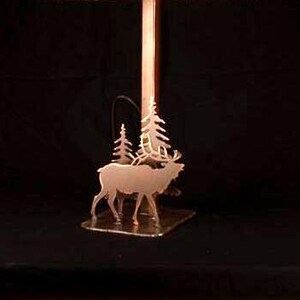 May include: A copper lamp base with a silhouette of two elk and pine trees. The base is a rectangular shape with a raised edge.