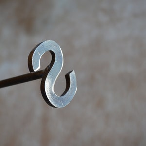 May include: A metal fireplace poker with a decorative S-shaped handle.
