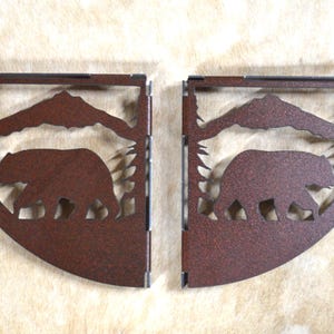 May include: Two rustic brown metal shelf brackets with a bear silhouette and mountain scene design.