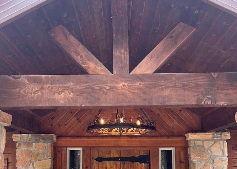 May include: A wooden front porch with a dark brown stained wood ceiling and a large wooden beam. The ceiling has a decorative wood trim and a black metal chandelier with a circular design.