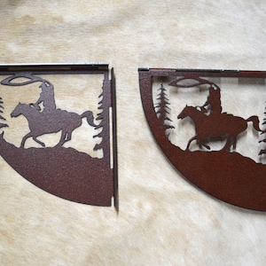 May include: Two rustic metal corner shelves with a cowboy riding a horse design. The shelves are a dark brown color and have a distressed finish.