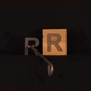 May include: Two wooden blocks with the letter "R" carved into them. The blocks are brown and have a natural wood finish. A metal hook is attached to the bottom of the blocks.