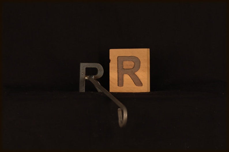 May include: Two wooden blocks with the letter "R" carved into them. The blocks are brown and have a natural wood finish. A metal hook is attached to the bottom of the blocks.