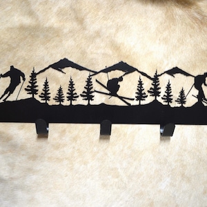 May include: Black metal ski-themed key rack with five hooks. The rack features a silhouette of skiers and mountains.
