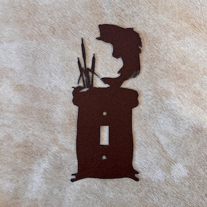 May include: A brown metal light switch cover featuring a leaping fish above a rectangular base. The design includes cattails and a small hole for the switch. The cover is designed to fit a standard light switch.