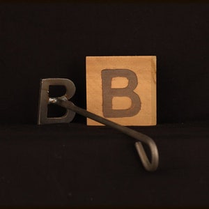 May include: A metal branding iron shaped like the letter "B" with a wooden block with the letter "B" on it.