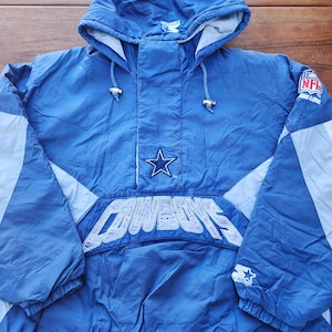 May include: A blue and white Starter brand NFL Dallas Cowboys jacket with a large embroidered logo on the front. The jacket has a hood and a zip closure.