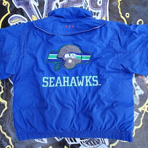 May include: A blue Seattle Seahawks jacket with the team logo and the word "SEAHAWKS" in white lettering. The jacket has a collar and a zipper. The NFL logo is embroidered on the collar.
