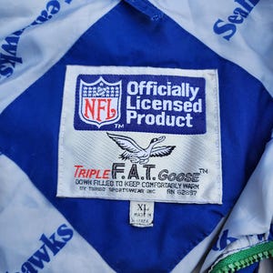 May include: Close-up of a blue and white Seahawks jacket interior. The jacket features a diamond-shaped blue panel with a white background. The NFL officially licensed product label is visible, along with the Triple F.A.T. Goose brand label.
