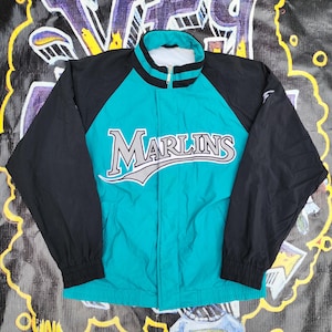 May include: A teal and black zip-up jacket with the word "Marlins" across the chest in white and gray lettering. The jacket has a stand-up collar and black sleeves. The jacket is a vintage sports apparel item.