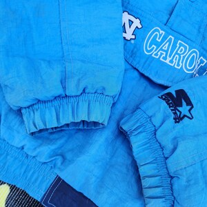 Puede incluir: Primer plano de una chaqueta azul claro con la palabra "CARO" en letras blancas. La chaqueta tiene pu&ntilde;os el&aacute;sticos y un logotipo de Starter con una estrella. La chaqueta est&aacute; hecha de un material brillante, posiblemente nailon.