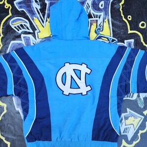 Puede incluir: Chaqueta con capucha azul claro con un gran logotipo blanco y azul claro en la espalda. La chaqueta tiene un dise&ntilde;o de bloques de color con paneles azul marino y azul claro. La chaqueta tiene cierre de cremallera y capucha con cord&oacute;n.
