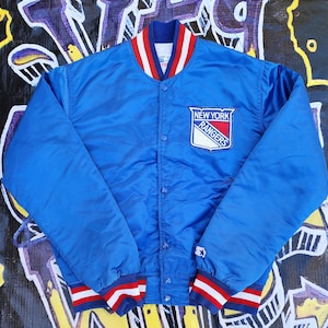 May include: A blue satin jacket with the New York Rangers logo patch on the chest. The jacket has a red, white, and blue striped collar and cuffs. The Starter logo is visible on the sleeve.
