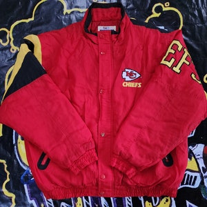 May include: Red, black, and yellow Kansas City Chiefs jacket with the team logo and "Chiefs" text on the front. The jacket has a zipper closure and a stand-up collar.