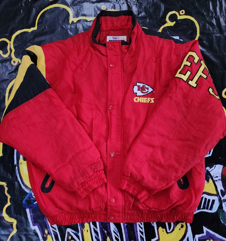 May include: Red, black, and yellow Kansas City Chiefs jacket with the team logo and "Chiefs" text on the front. The jacket has a zipper closure and a stand-up collar.
