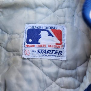 May include: A white label with blue and red trim, featuring a baseball player silhouette and the text "Official Licensee Major League Baseball by Starter New Haven, CT".