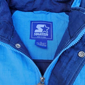 Puede incluir: Chaqueta Starter vintage en tonos azules. La chaqueta presenta una cremallera frontal, una capucha y el logotipo de Starter en la etiqueta y el tirador de la cremallera. Fabricada en nailon y poli&eacute;ster.